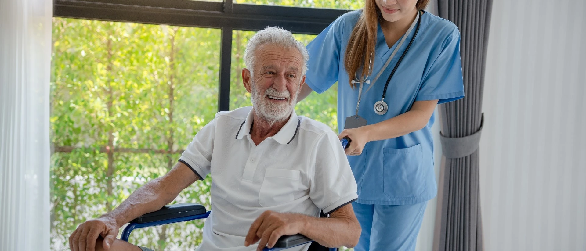 Elderly man in a wheelchair pushed by a nurse with custom drapery in the background,drapery and roller shades supplied by GOLDEN AGE HOUSING PRODUCTS